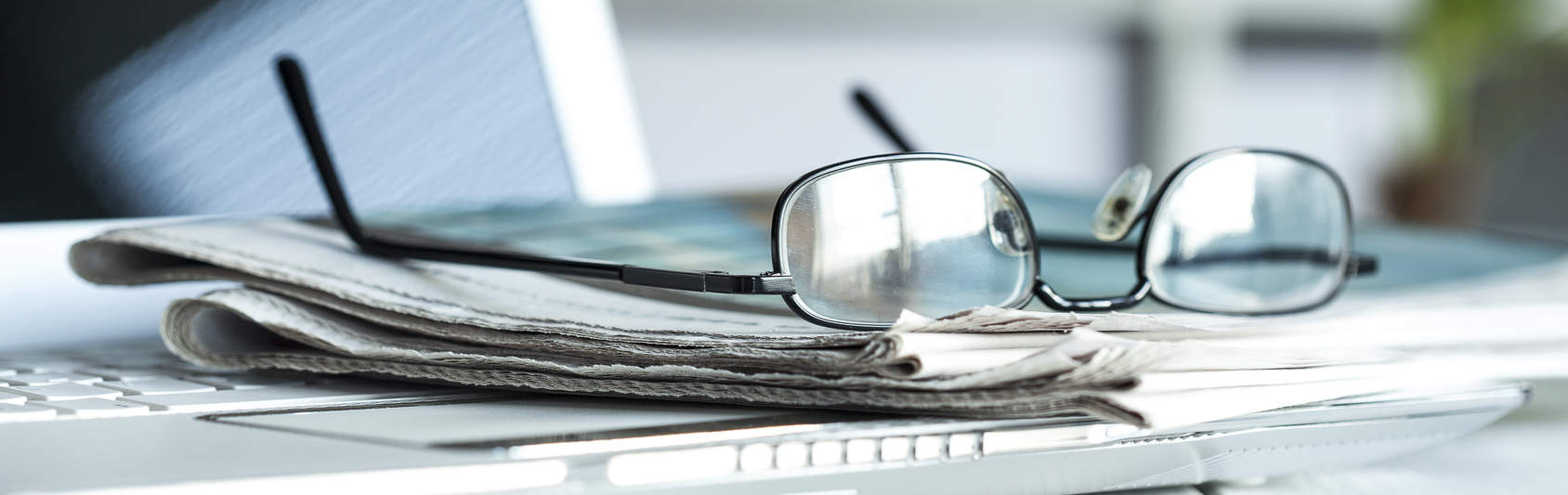 Lesebrille auf Zeitung und Laptop - bildlich für Publikationen der Versicherungsberater und Rentenberater